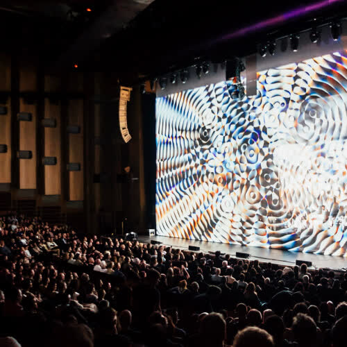 Audience contemplating Cardano Circles animation during Max Cooper's performance at Barbican Centre Hall in London.