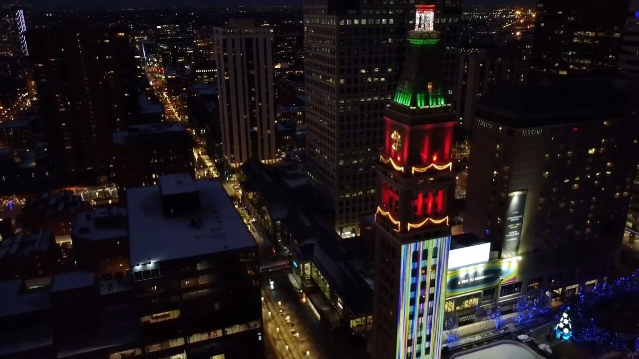 Projection of digital artwork displayed on a tall clock tower at night, blending vibrant colors and patterns with the architectural structure.