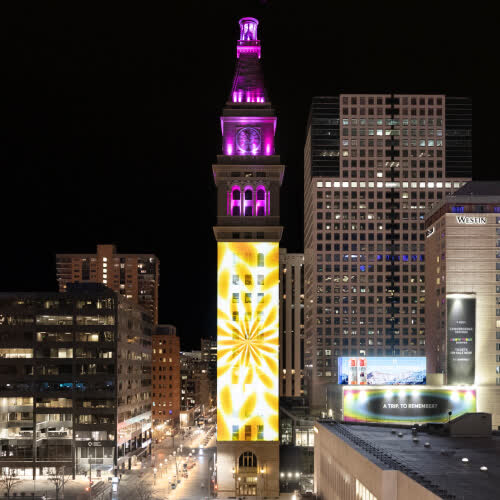 Projection of artwork displayed on a tall clock tower at night.